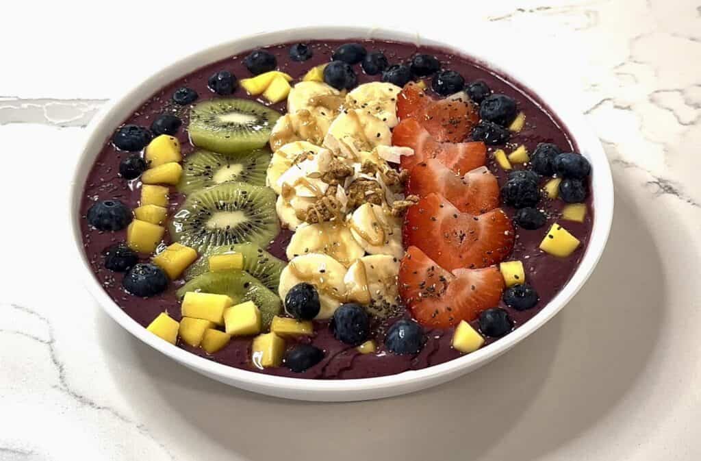 Homemade açaí bowl topped with strawberries, bananas, kiwi, blueberries, mango, granola, coconut, and honey drizzle.
