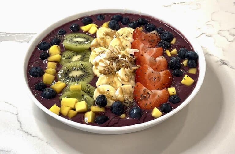 Homemade açaí bowl topped with strawberries, bananas, kiwi, blueberries, mango, granola, coconut, and honey drizzle.
