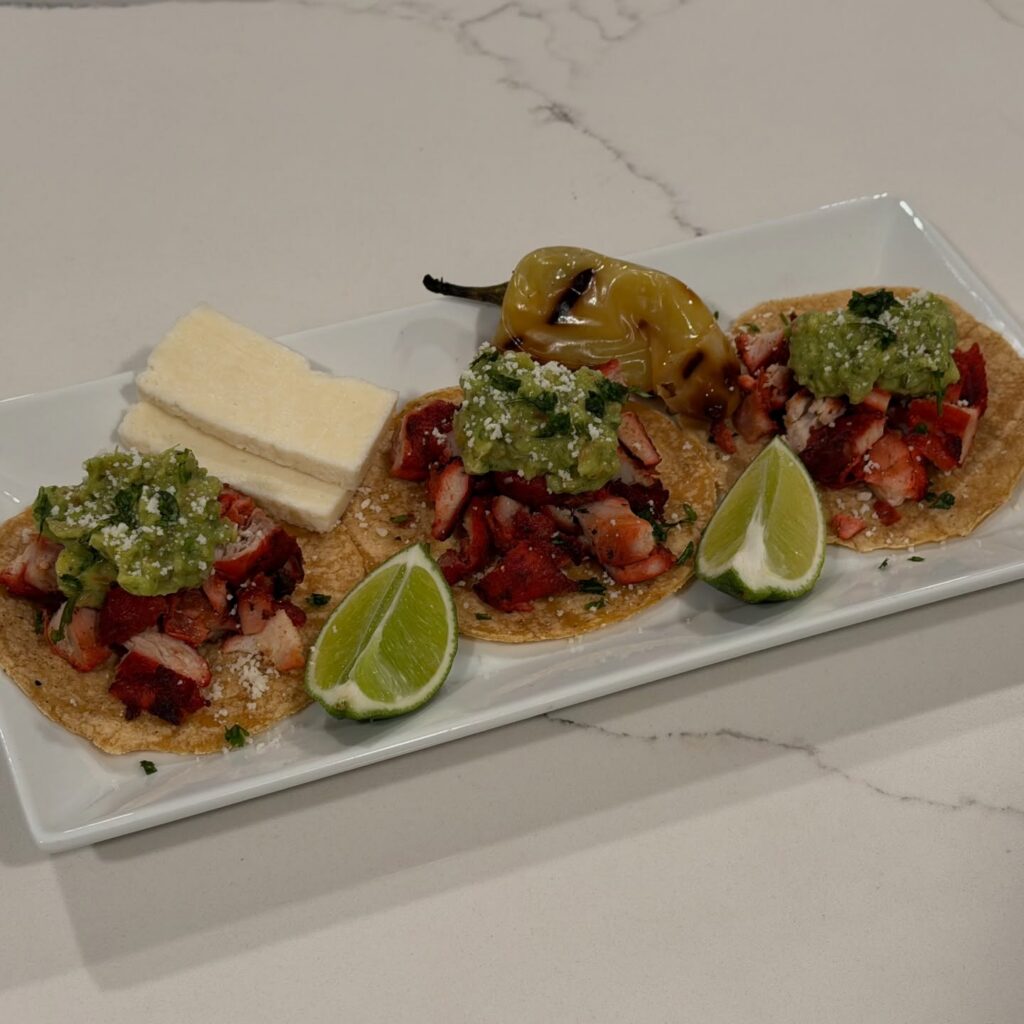 Homemade adobada street tacos with seasoned pork, salsa verde, cotija cheese, grilled güero pepper, lime wedges, and warm corn tortillas.