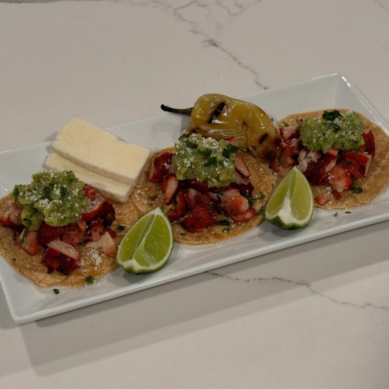 Homemade adobada street tacos with seasoned pork, salsa verde, cotija cheese, grilled güero pepper, lime wedges, and warm corn tortillas.