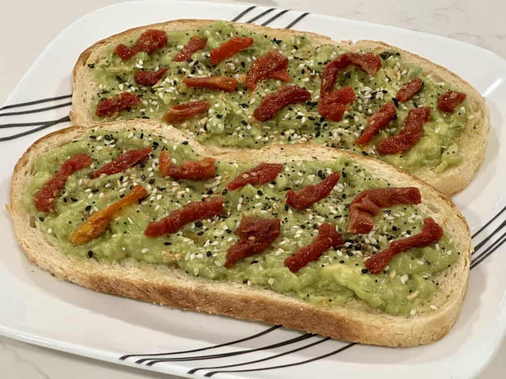 Homemade avocado toast topped with sun-dried tomatoes and everything bagel seasoning on toasted bread.