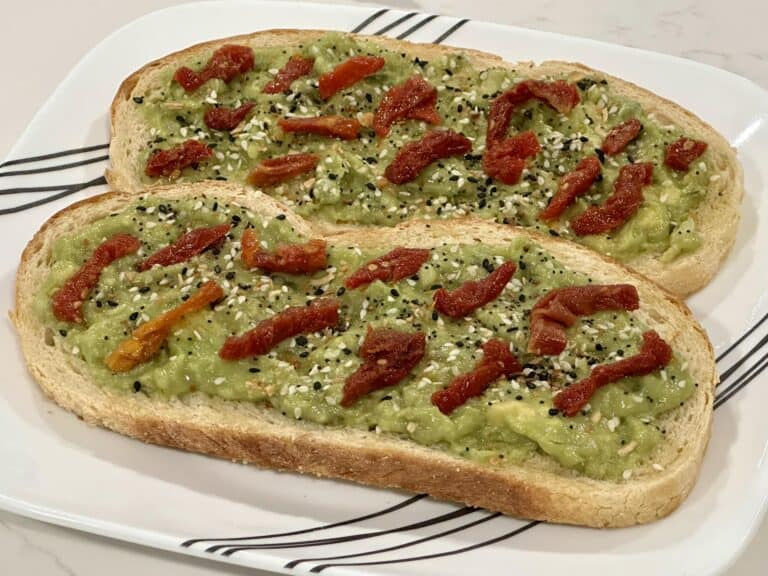 Homemade avocado toast topped with sun-dried tomatoes and everything bagel seasoning on toasted bread.