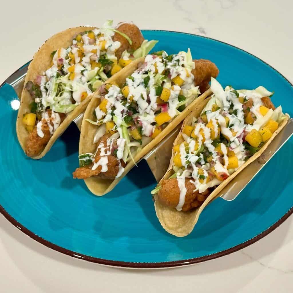 Beer Battered Fish Tacos with Mango Salsa Reynaldos Cocina Beer battered fish tacos topped with mango salsa, cabbage, and crema on corn tortillas.