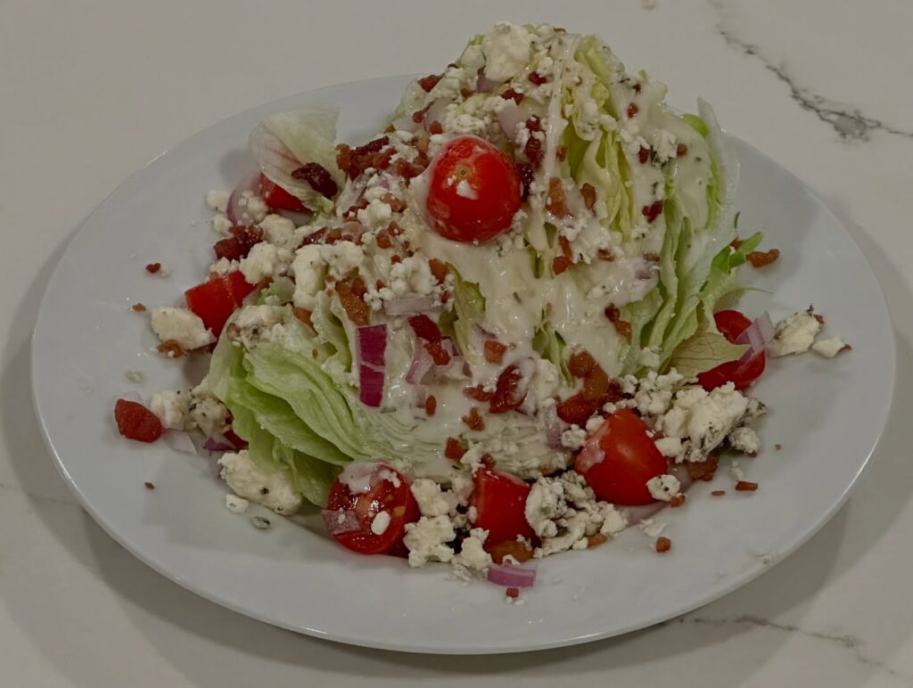 Blue Cheese Wedge Salad Reynaldos Cocina Blue cheese wedge salad topped with applewood smoked bacon, blue cheese crumbles, cherry tomatoes, red onion, and buttermilk ranch dressing.