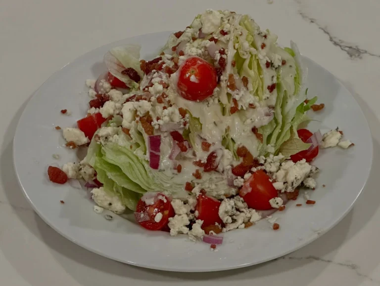Blue cheese wedge salad topped with applewood smoked bacon, blue cheese crumbles, cherry tomatoes, red onion, and buttermilk ranch dressing.