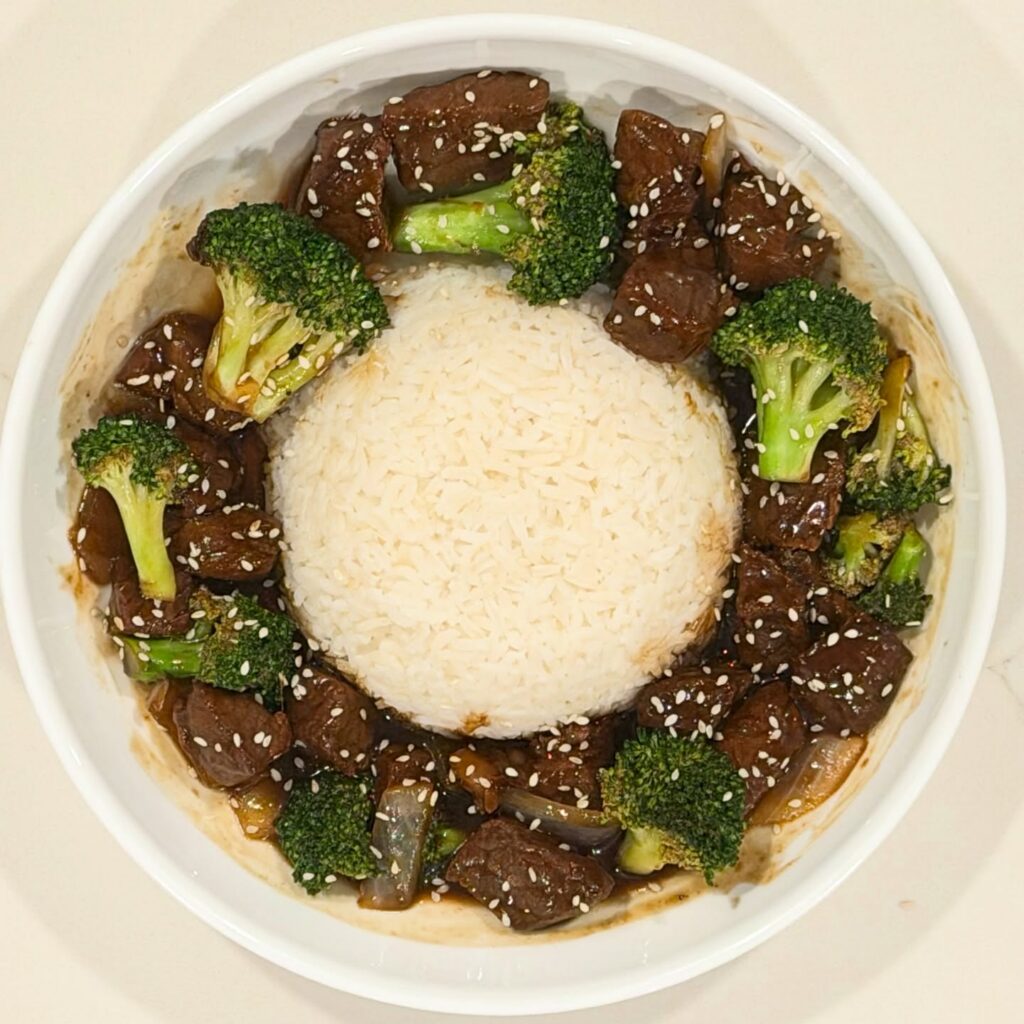 Homemade broccoli beef with cubed ribeye simmered in a savory soy ginger sauce with broccoli, onions, sesame seeds, and served over jasmine rice.