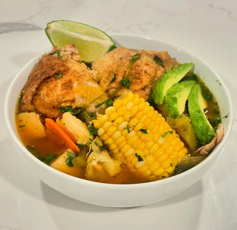 Homemade Caldo de Pollo chicken soup with corn, potatoes, carrots, avocado, and lime served in a white bowl from Reynaldo’s Cocina