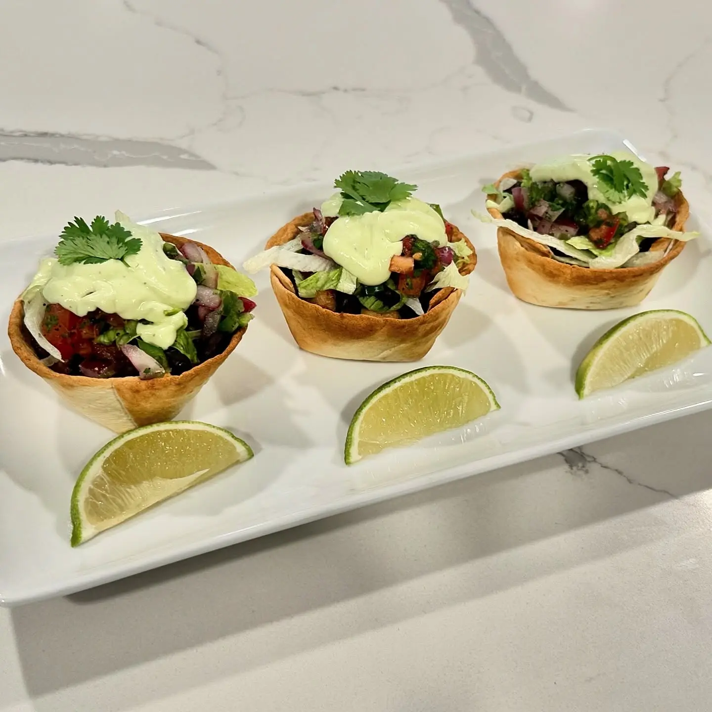 Cantina chicken taco cups filled with seasoned chicken, black beans, lettuce, pico de gallo, avocado crema, cilantro, and lime wedges.