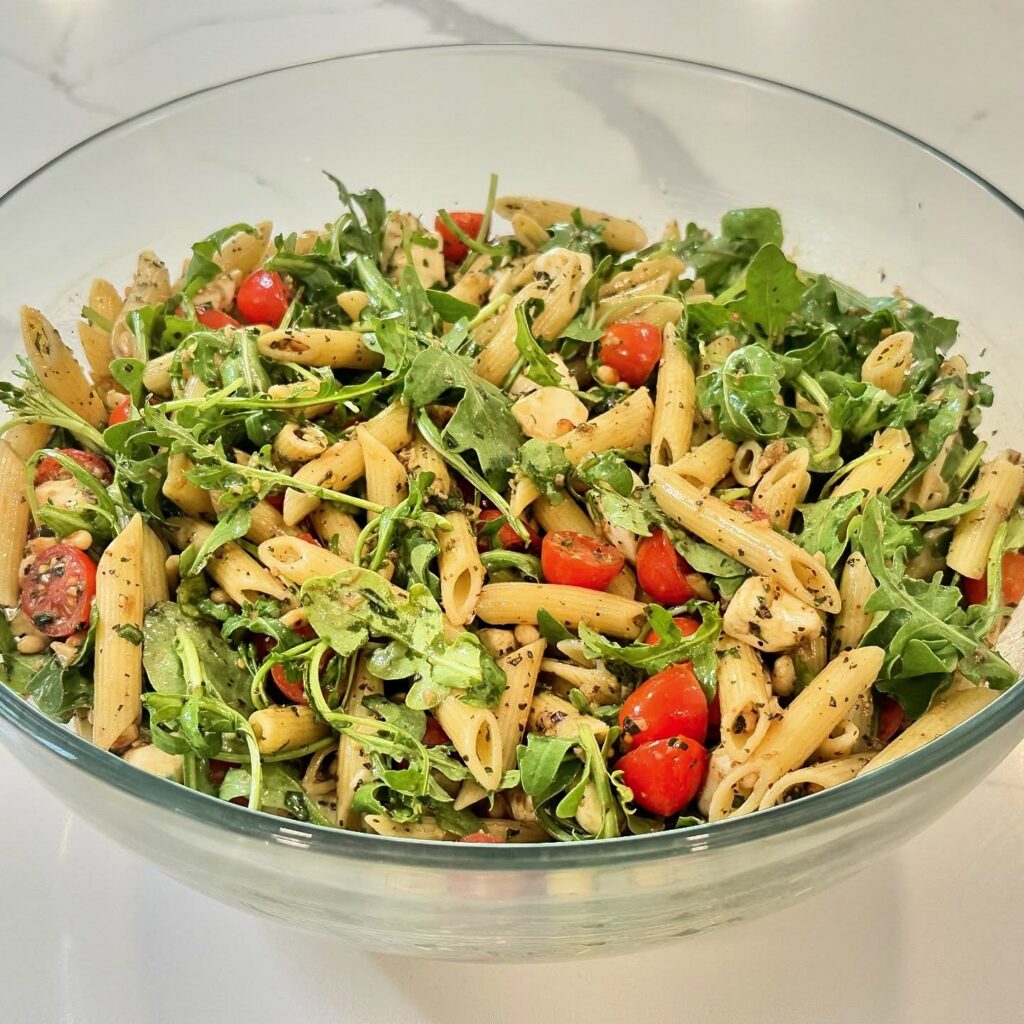 Caprese pasta salad with rotini pasta, cherry tomatoes, fresh mozzarella, arugula, basil, pine nuts, Parmesan, and balsamic glaze.