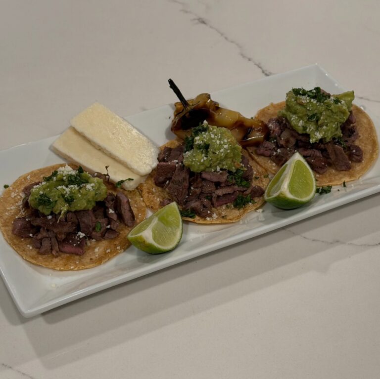 Homemade Carne Asada Street Tacos with citrus marinated steak, salsa verde, cotija cheese, grilled pepper, lime wedges, and warm corn tortillas.
