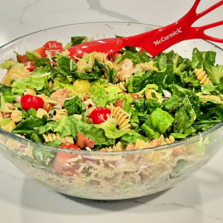 Chicken Caesar pasta salad with grilled chicken, romaine lettuce, rotini pasta, bacon, cherry tomatoes, red onion, and Parmesan cheese.
