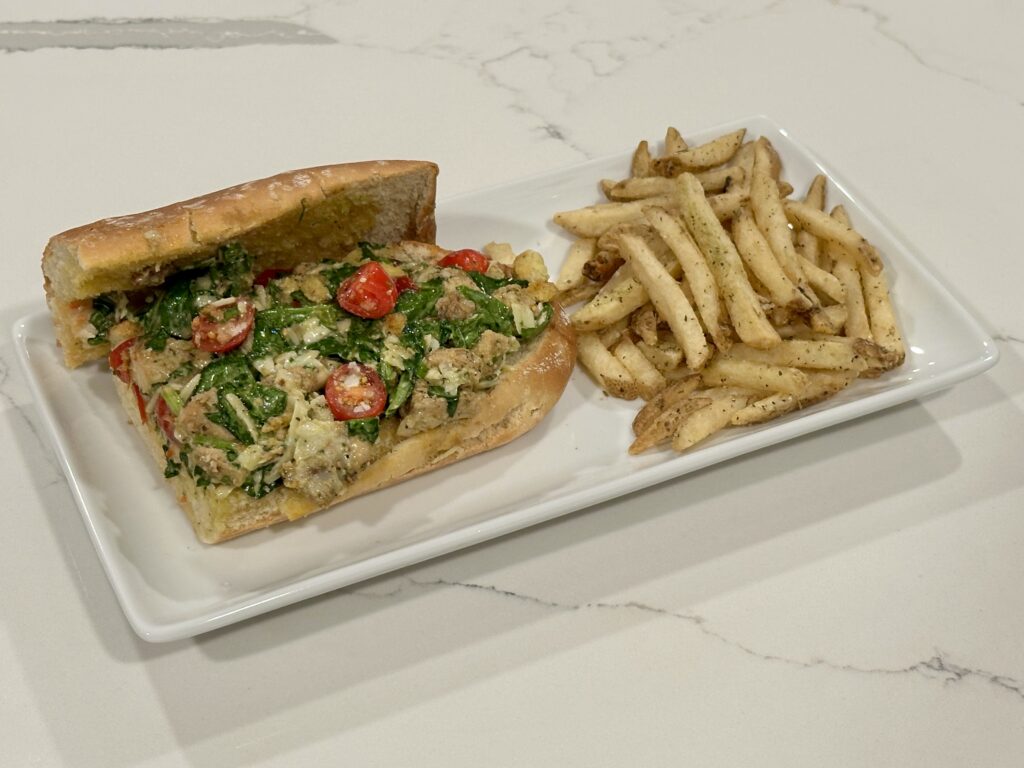 Chicken Caesar Sandwich Chicken Caesar Sandwich with romaine lettuce, Parmesan cheese, tomatoes, croutons, and garlic fries on the side.
