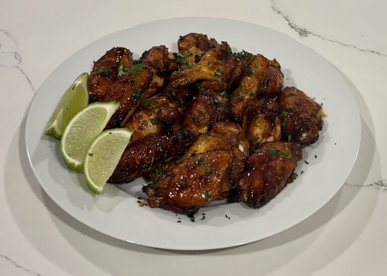 Delicious glazed chicken wings with lime wedges on a white plate.