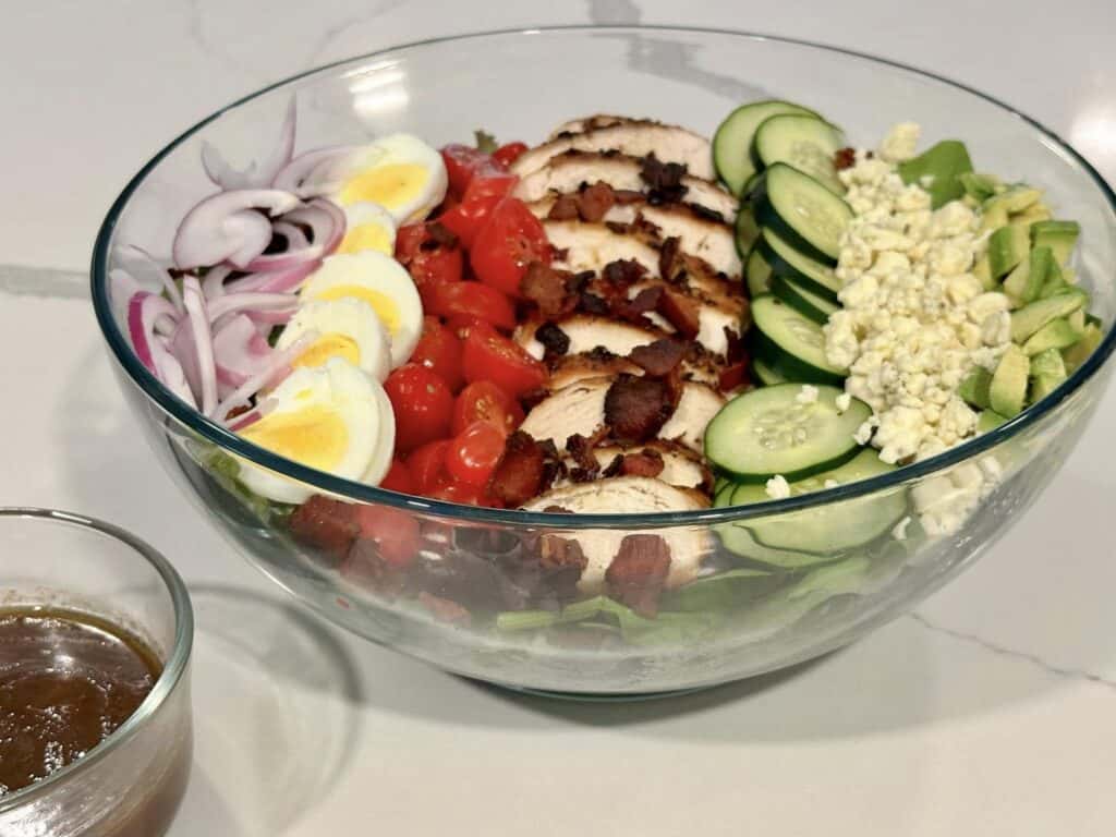 Homemade Cobb salad with grilled chicken, bacon, avocado, cucumber, tomatoes, egg, red onion, blue cheese, and balsamic dressing.