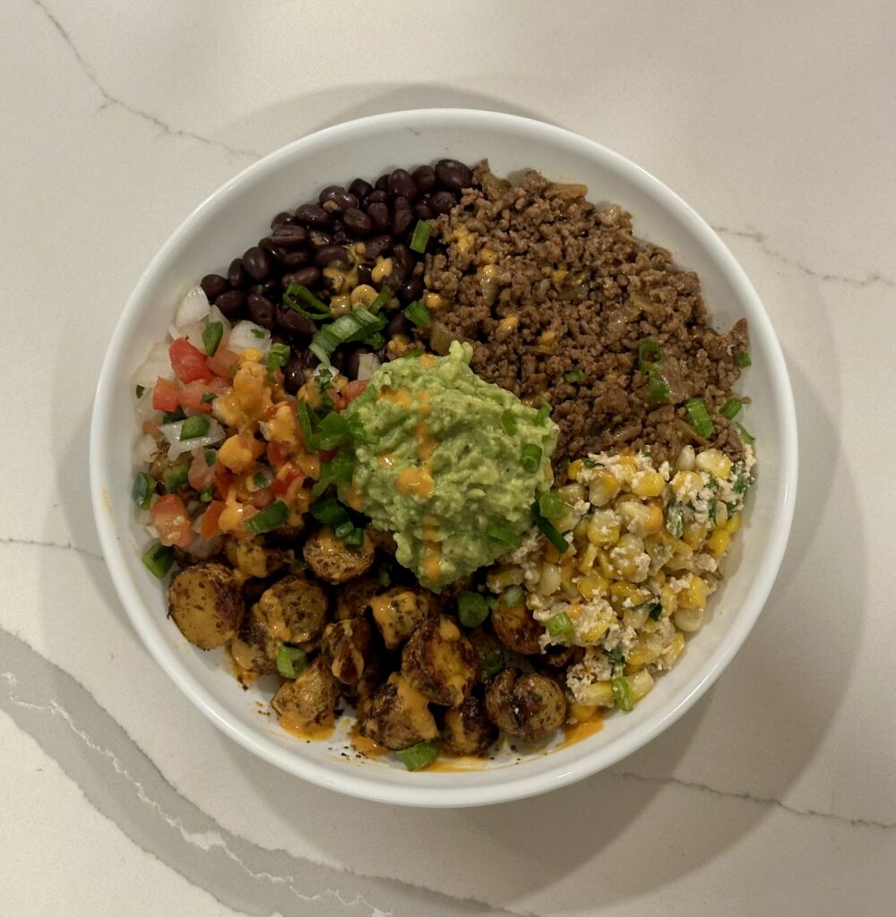 Fiesta Potato Taco Bowl with crispy baby gold potatoes, taco meat, black beans, homemade elote salad, pico de gallo, guacamole, and chipotle crema.