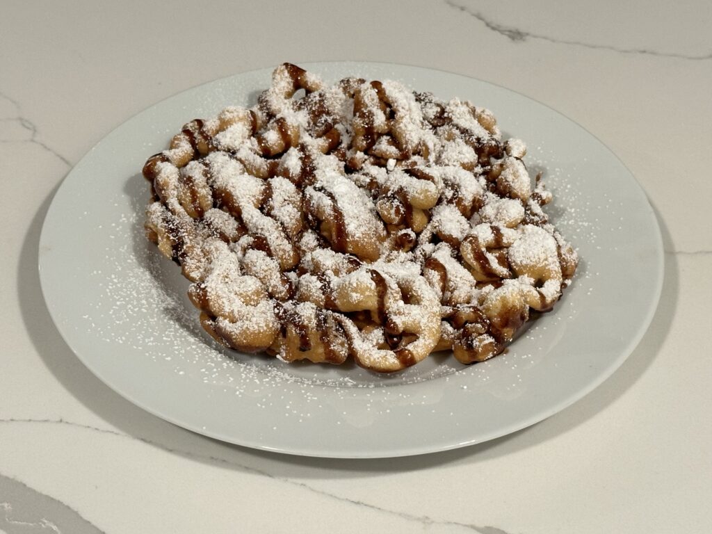 Classic Funnel Cake topped with powdered sugar and chocolate drizzle on a white plate.