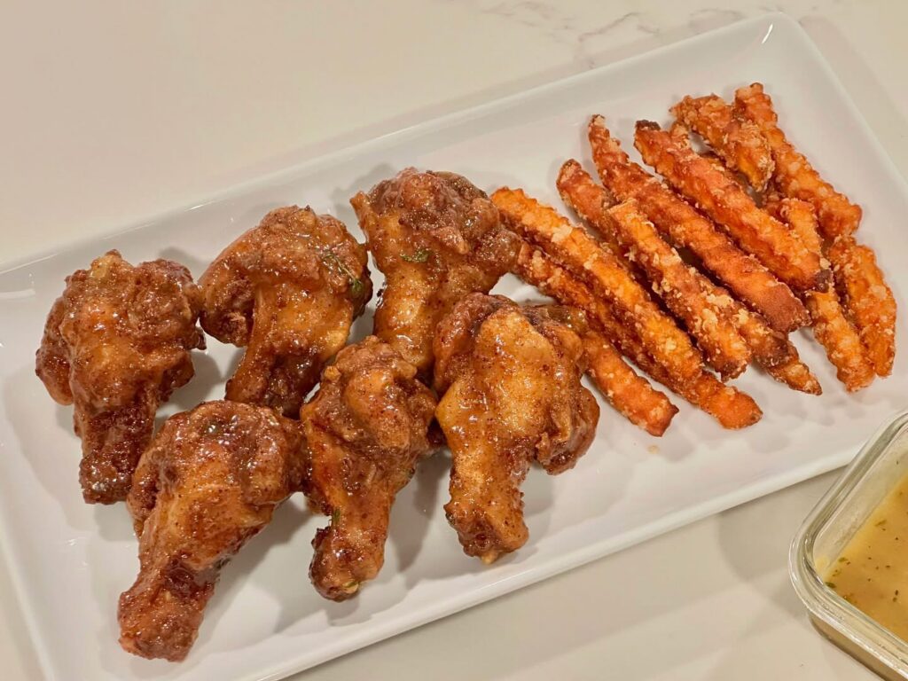 Golden maple glazed chicken wings with crispy sweet potato fries on a white serving platter by Reynaldo’s Cocina