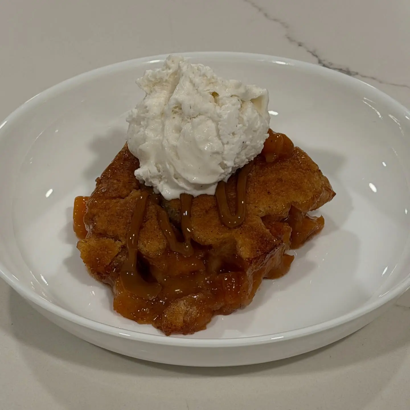 Homemade peach cobbler baked until golden and finished with caramel drizzle and French vanilla ice cream.