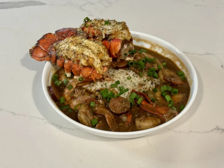 Lobster Gumbo with lobster tail, Cajun chicken, andouille sausage, white rice, and green onions.