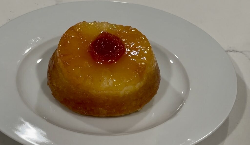 Mini pineapple upside down cake with caramelized pineapple and cherry on a white plate.