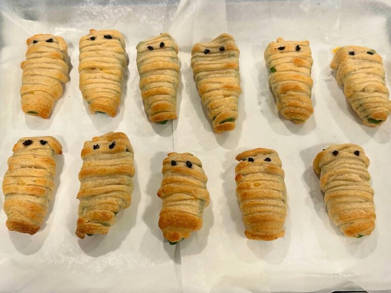 Homemade Mummy Jalapeño Poppers stuffed with cream cheese, cheddar cheese, and bacon then wrapped in crescent dough strips with black olive eyes.