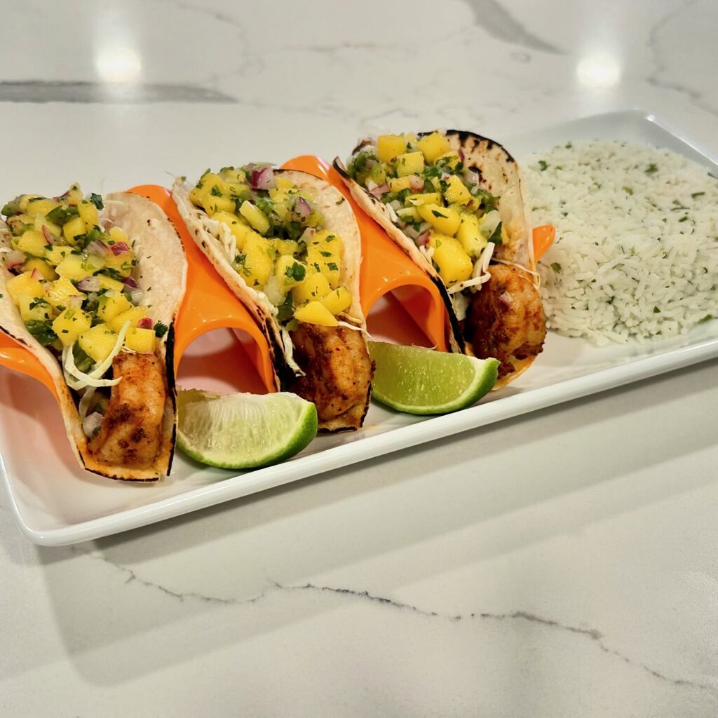 Shrimp tacos topped with mango salsa and shredded cabbage served with cilantro lime rice and lime wedges.