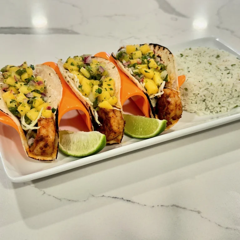 Shrimp tacos topped with mango salsa and shredded cabbage served with cilantro lime rice and lime wedges.