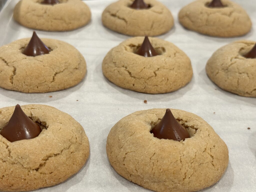 Soft peanut butter cookies rolled in sugar and topped with Hershey's Kisses on a baking sheet.