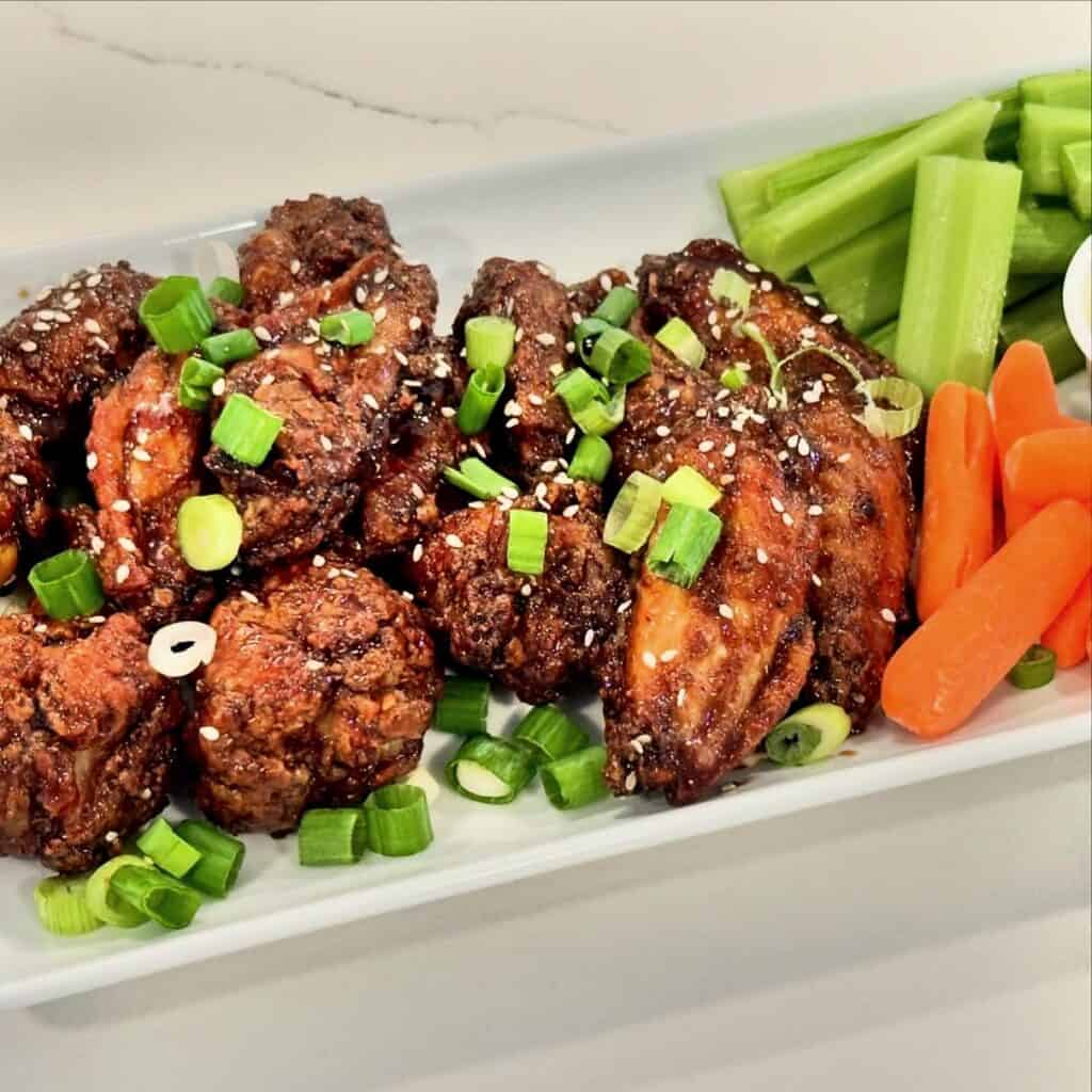 Homemade sesame teriyaki chicken wings topped with green onions and sesame seeds served with celery and carrots.