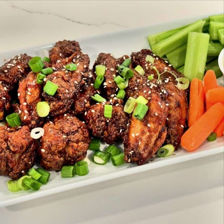 Homemade sesame teriyaki chicken wings topped with green onions and sesame seeds served with celery and carrots.