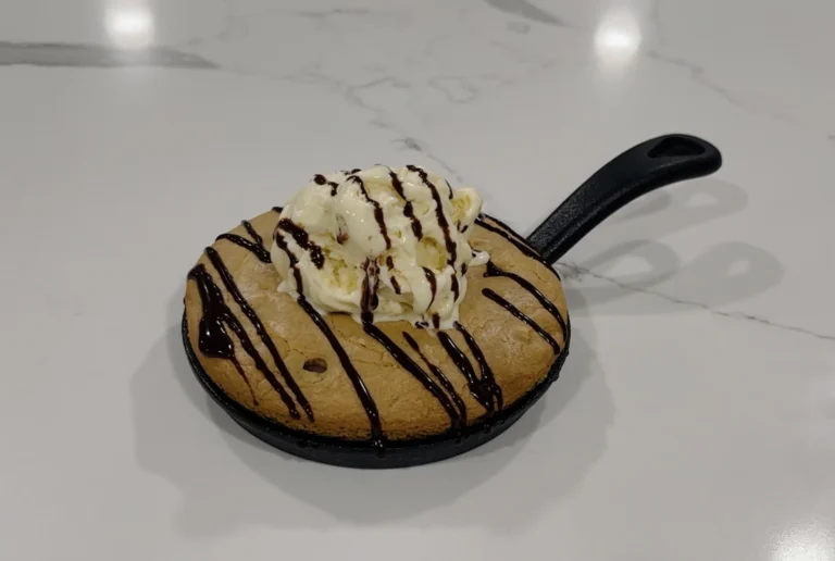 Warm skillet sugar cookie topped with vanilla bean ice cream and chocolate drizzle served in a cast iron skillet.