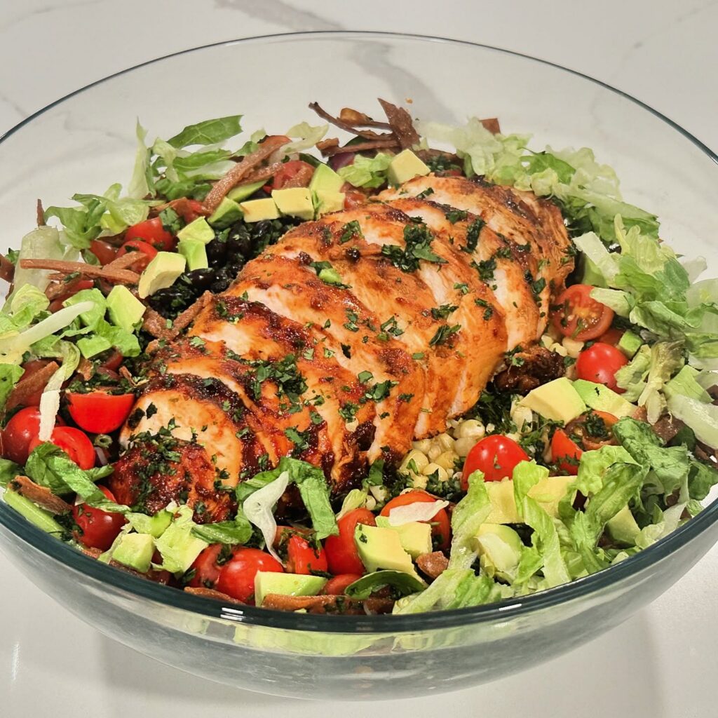 Southwest BBQ chicken salad with grilled chicken, romaine, spinach, black beans, corn, tomatoes, avocado, tortilla strips, and cilantro.
