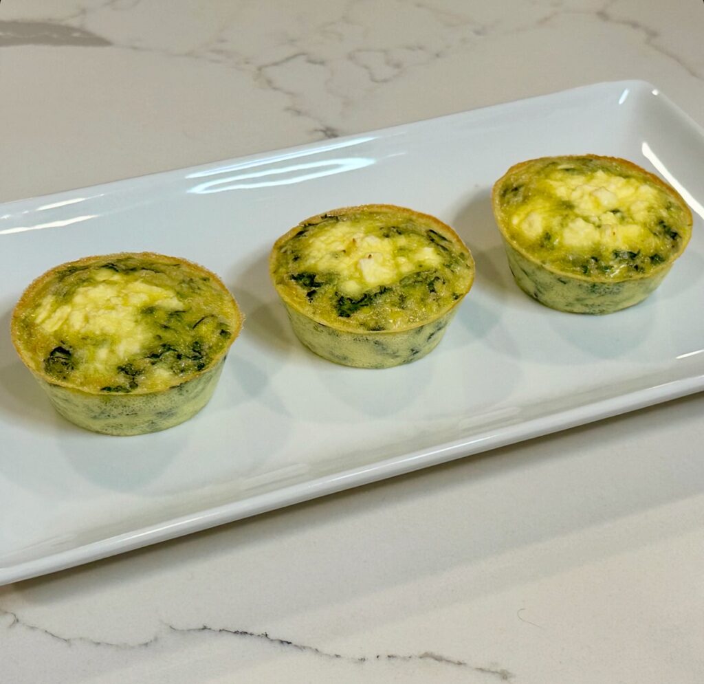 Spinach and feta egg cups baked in muffin tins and served on a white platter.