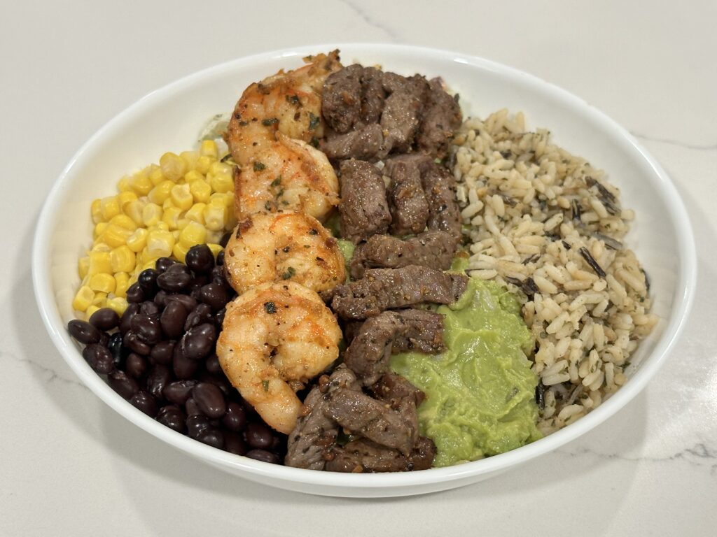 Steak and Shrimp Protein Bowl with wild rice, black beans, corn, guacamole, seasoned steak, and garlic shrimp.