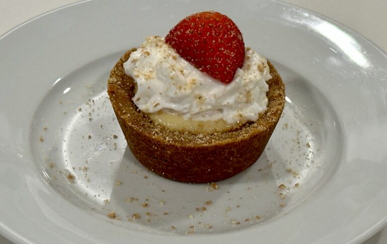 Strawberry Cheesecake Bite topped with whipped cream, fresh strawberry, and graham cracker crumbs.