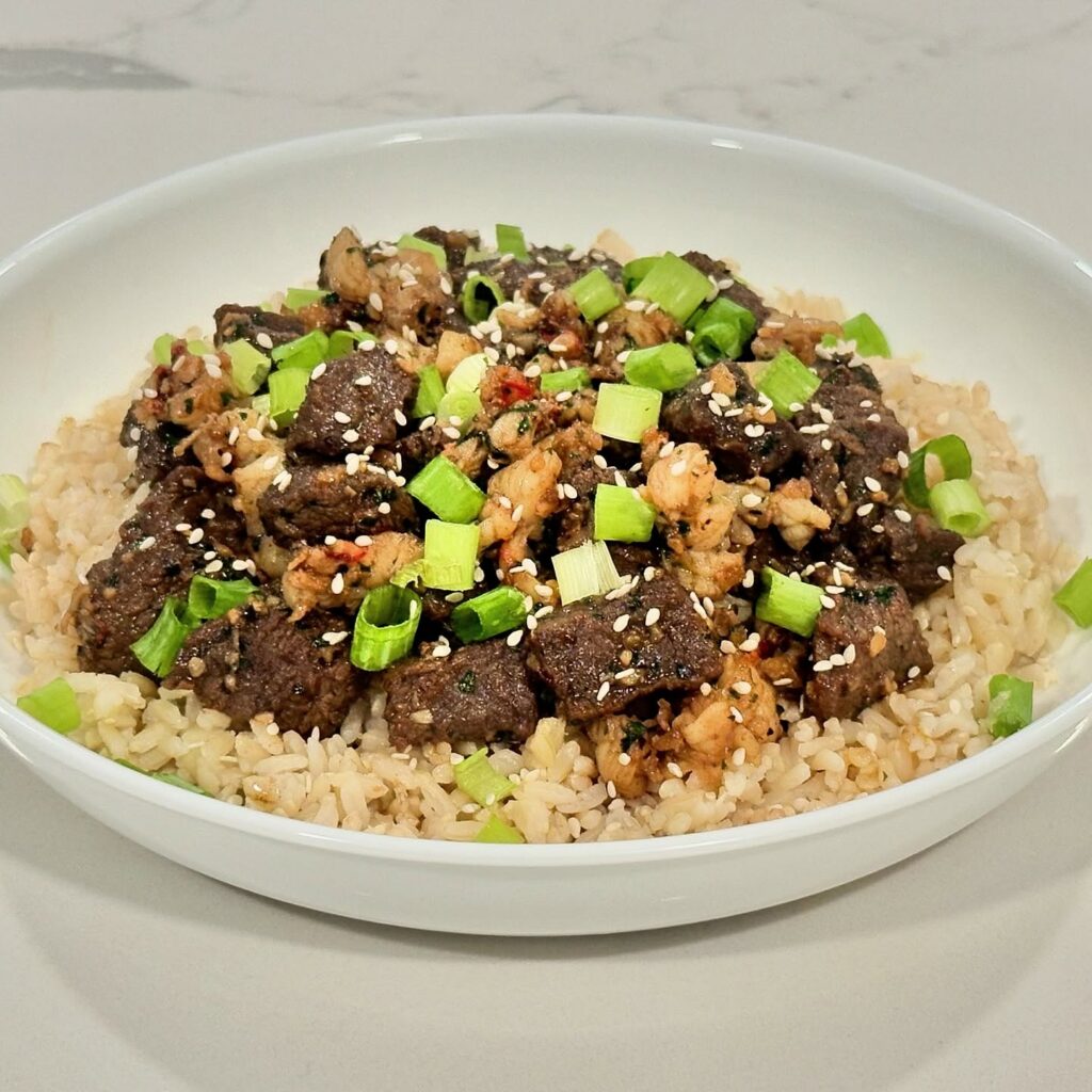 Surf and turf protein bowl with steak, lobster, brown rice, green onions, sesame seeds, garlic, and teriyaki sauce.