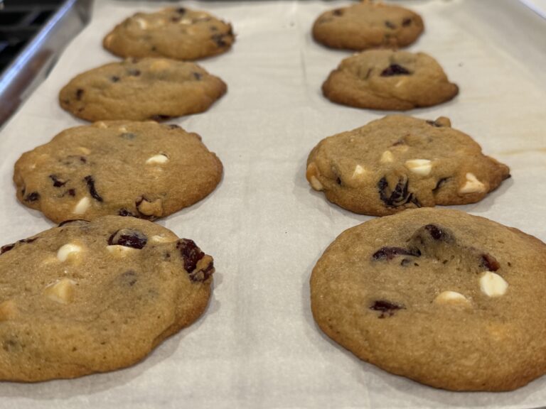Soft baked white chocolate cranberry cookies with orange zest cooling on a baking sheet.