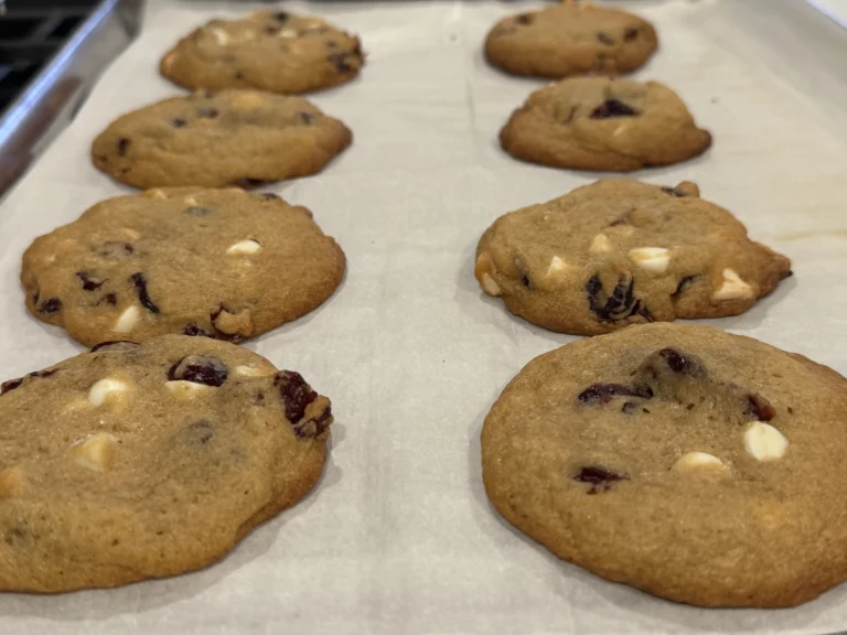 Soft baked white chocolate cranberry cookies with orange zest cooling on a baking sheet.