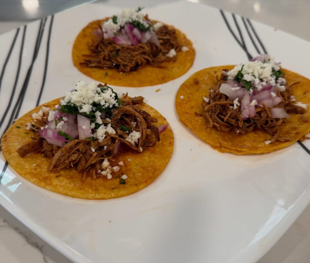 Crockpot chipotle chicken street tacos topped with red onion, cilantro, and cotija cheese on warm corn tortillas.