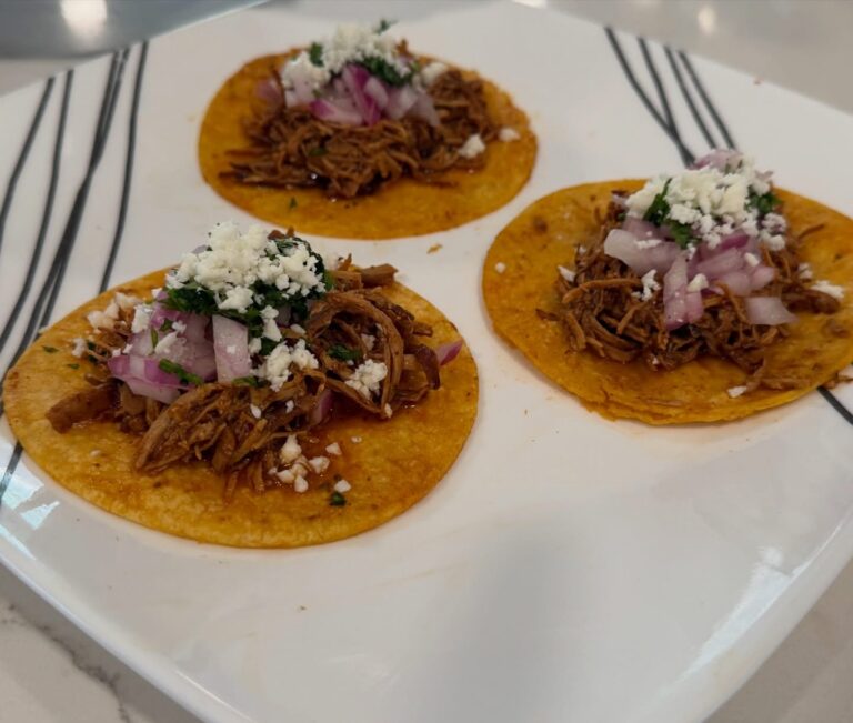 Crockpot chipotle chicken street tacos topped with red onion, cilantro, and cotija cheese on warm corn tortillas.