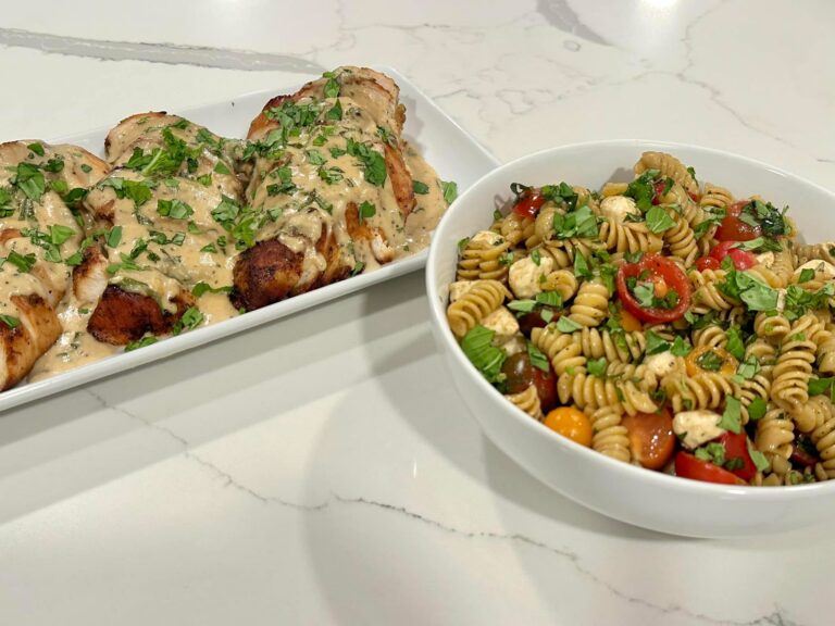 Blackened chicken breasts topped with creamy basil Parmesan sauce served with homemade pasta salad featuring mozzarella pearls, cherry tomatoes, basil, and vinaigrette.