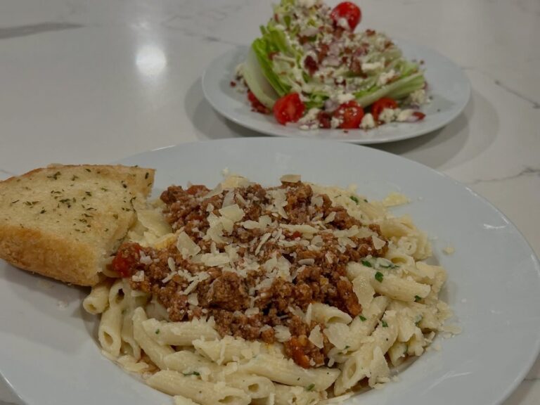 Creamy Million Dollar Penne topped with homemade Italian sausage meat sauce, Parmesan cheese, garlic bread, and wedge salad.